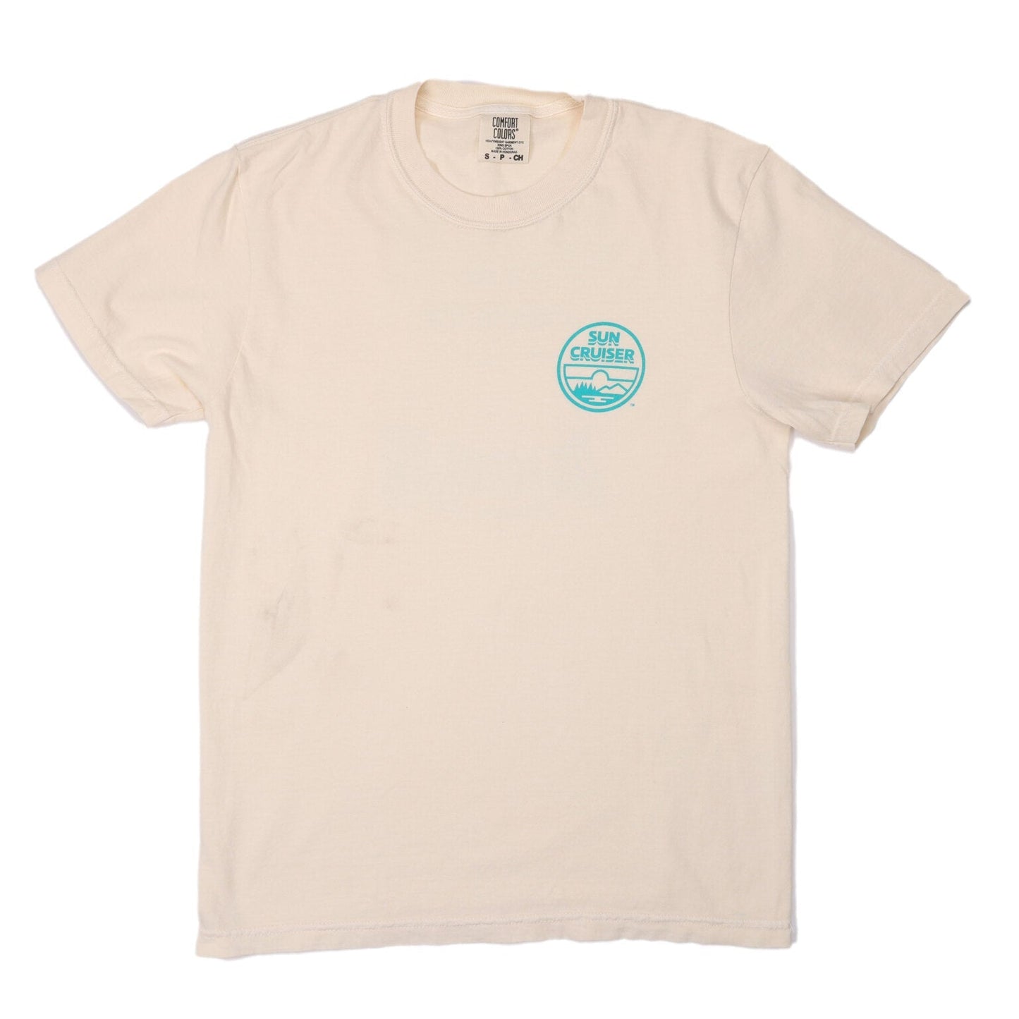 A flat lay of a plain cream-colored short-sleeved t-shirt. On the left chest, there is a small circular logo in teal. The logo features the words 'SUN CRUISER' and a stylized depiction of mountains and water.