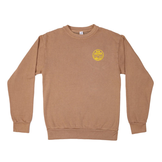 A flat lay of a light brown crewneck sweatshirt. On the left chest, there's a circular yellow logo that reads 'SUN CRUISER' in a stacked format. The logo also contains a small illustration of a landscape with mountains, water, and trees.