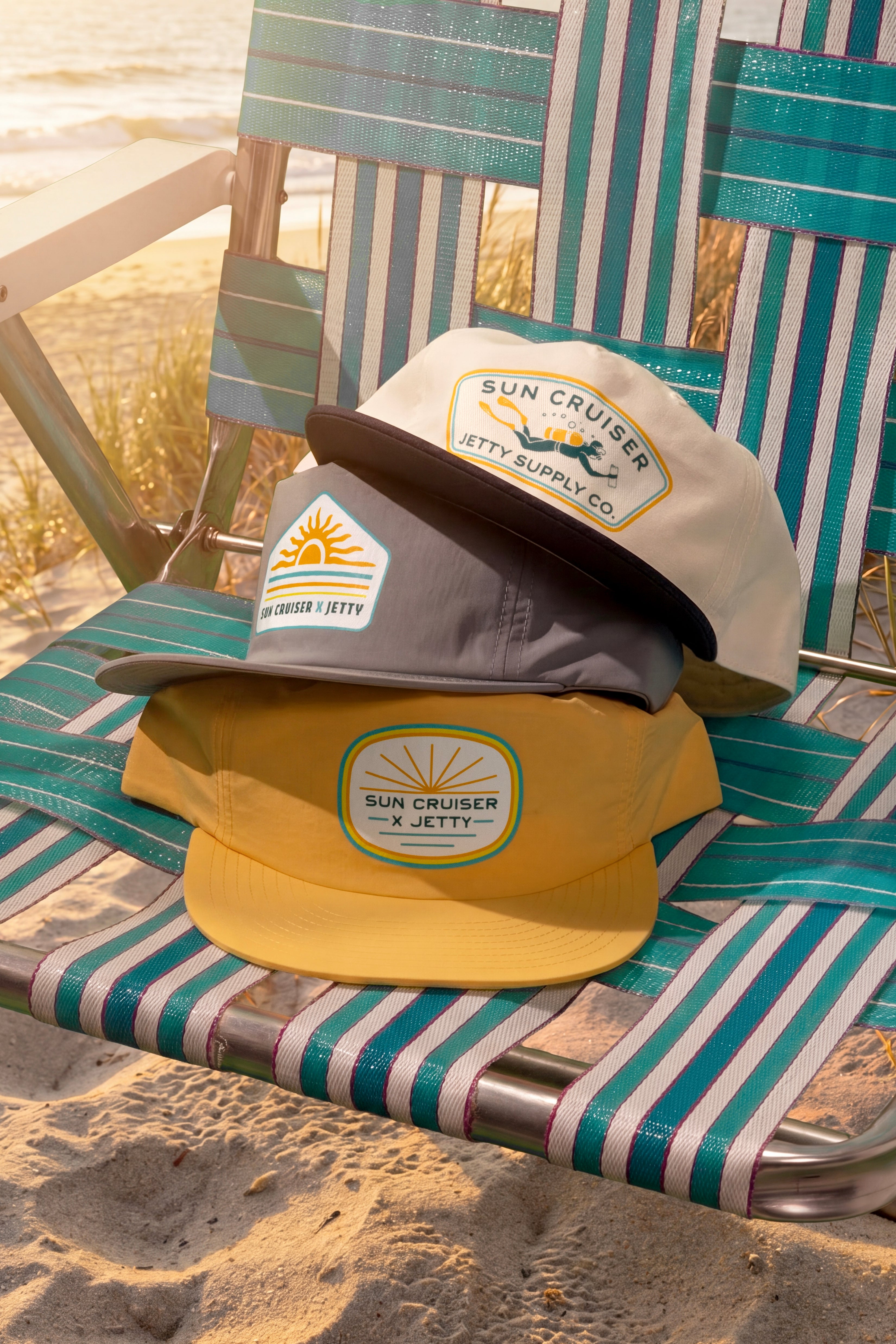 Two hats, one yellow and one gray, with branding on a striped beach chair.