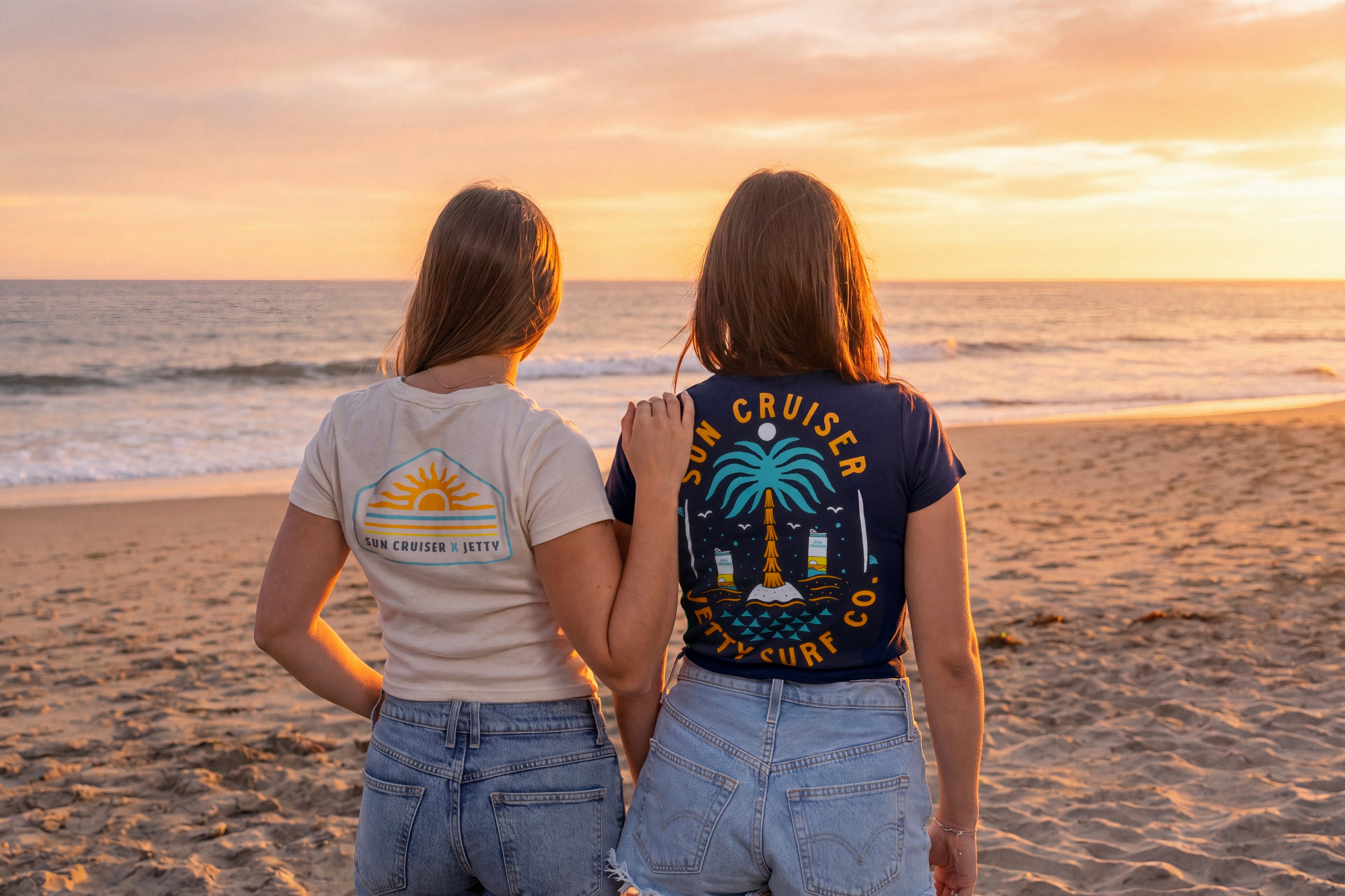 Two people on a beach at sunset, wearing t-shirts with 'Sun Cruiser' designs.