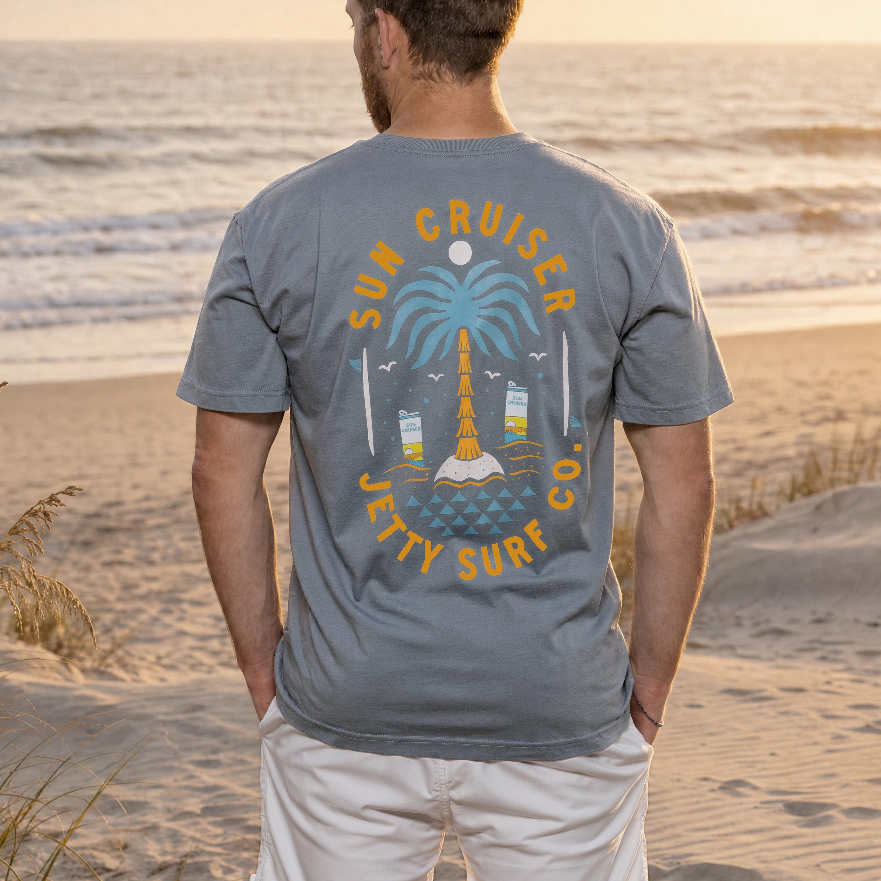 Man wearing a 'Sun Cruiser Jetty Surf Co.' t-shirt on a beach