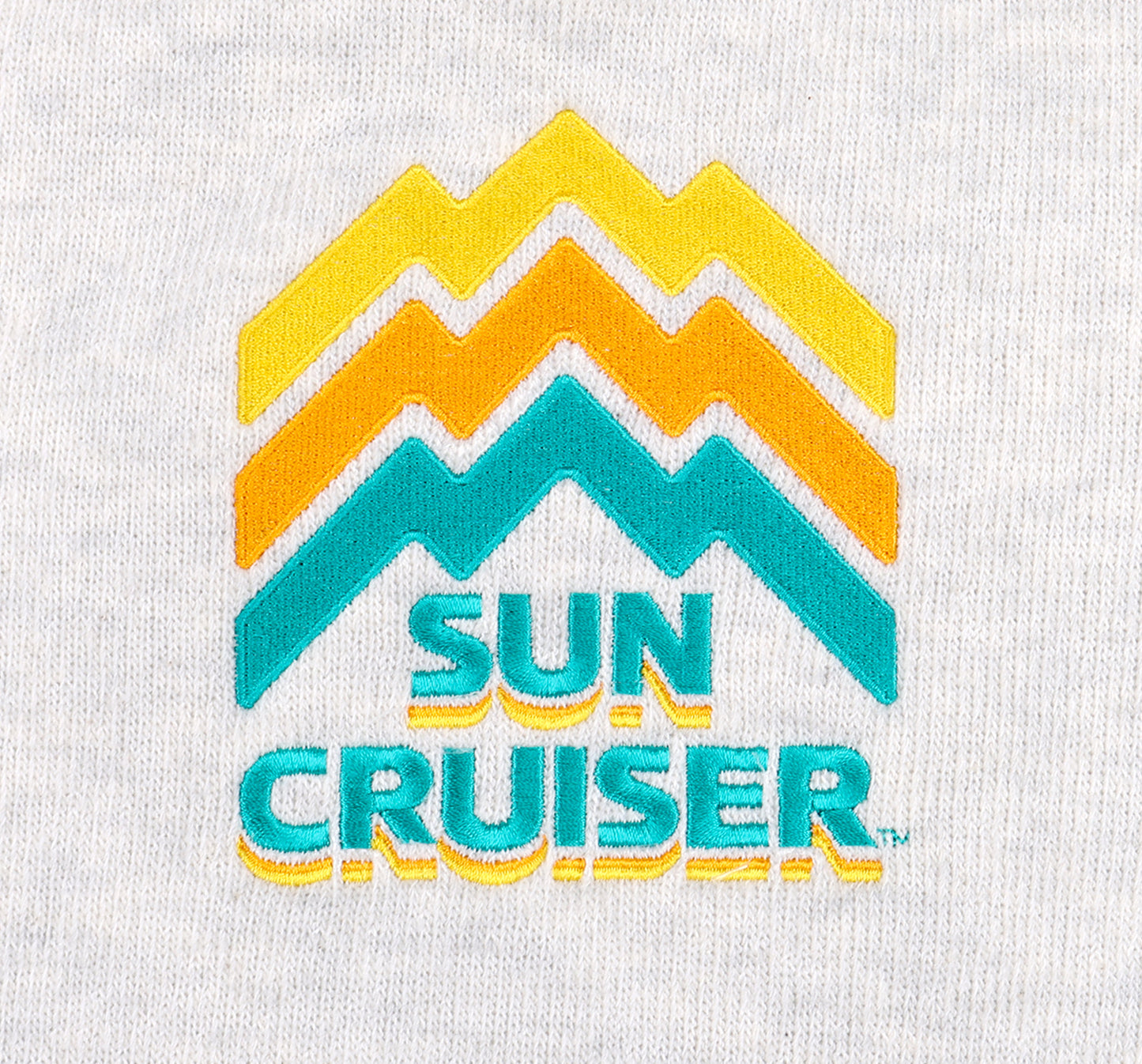 Close up of the centered embroidery logo on a Cream-colored Sun Cruiser Crewneck Sweatshirt. Line work on the logo is designed to look like a mountain range, in classic sun cruiser colors cyan, orange, and yellow