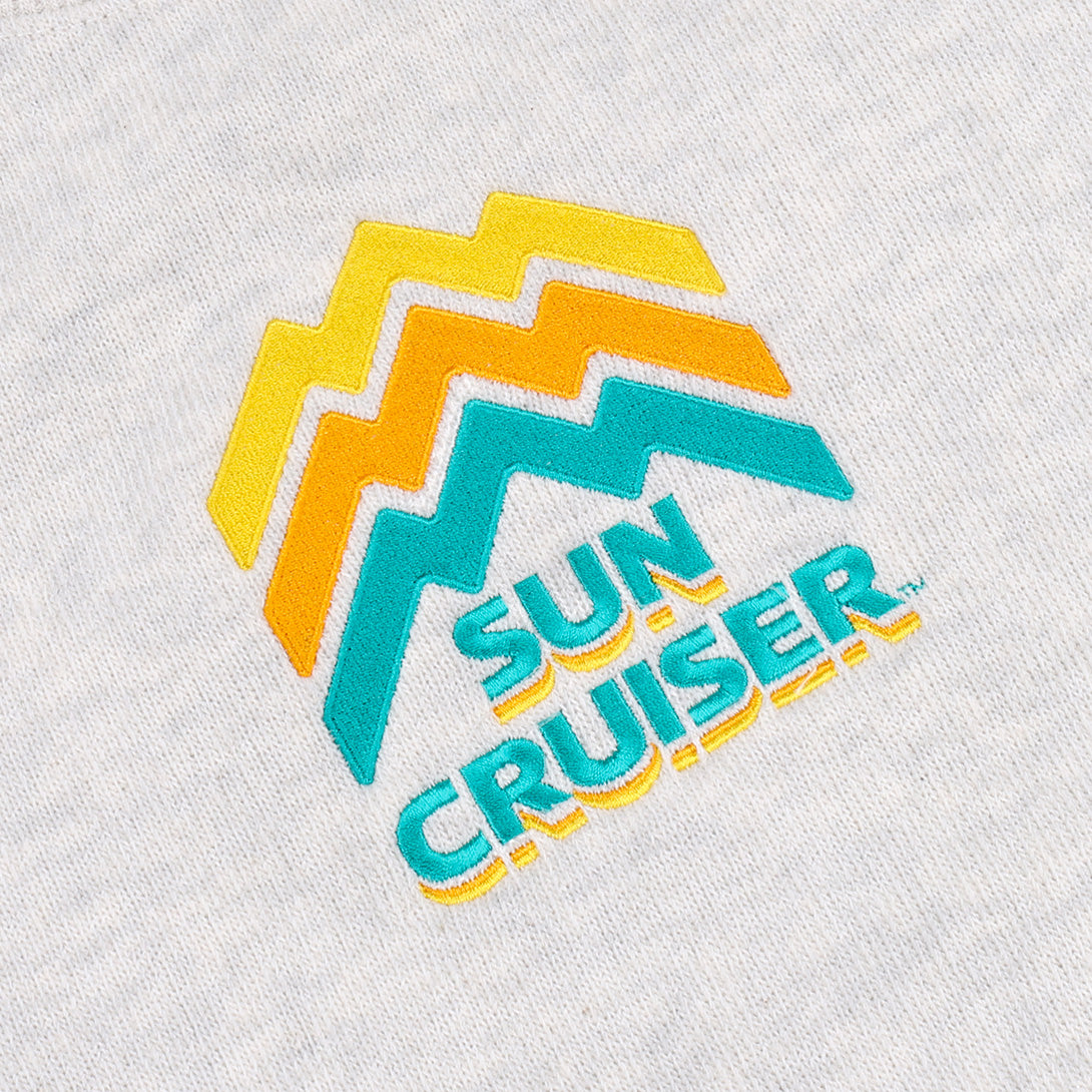 Close up of the centered embroidery logo on a Cream-colored Sun Cruiser Crewneck Sweatshirt. Line work on the logo is designed to look like a mountain range, in classic sun cruiser colors cyan, orange, and yellow
