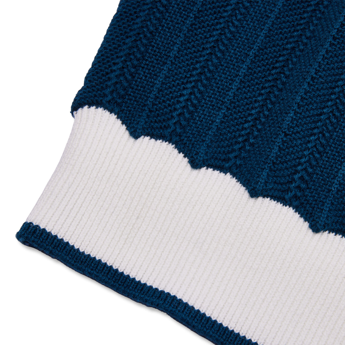 Close-up of a knit garment showing a dark navy blue ribbed textured section above a wide white ribbed cuff, on a plain white background.