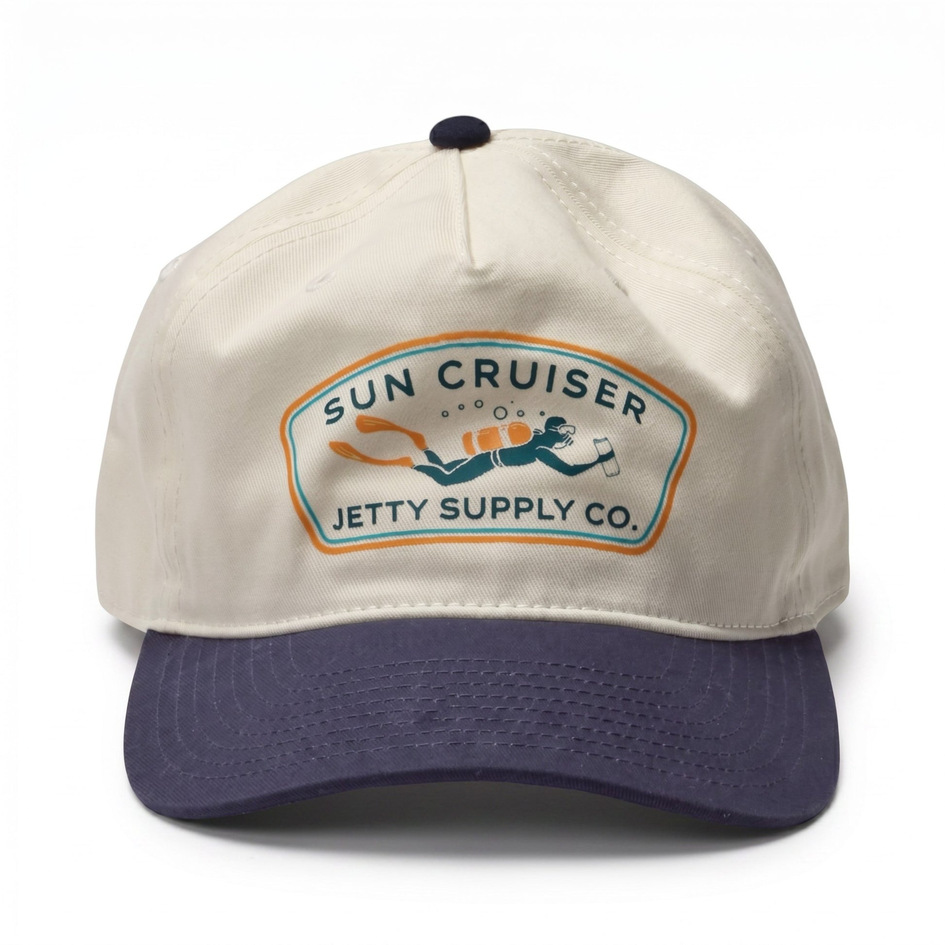 A baseball cap with an off-white crown and a dark navy blue curved brim. The front features a vintage-style embroidered patch that reads 'SUN CRUISER JETTY SUPPLY CO.