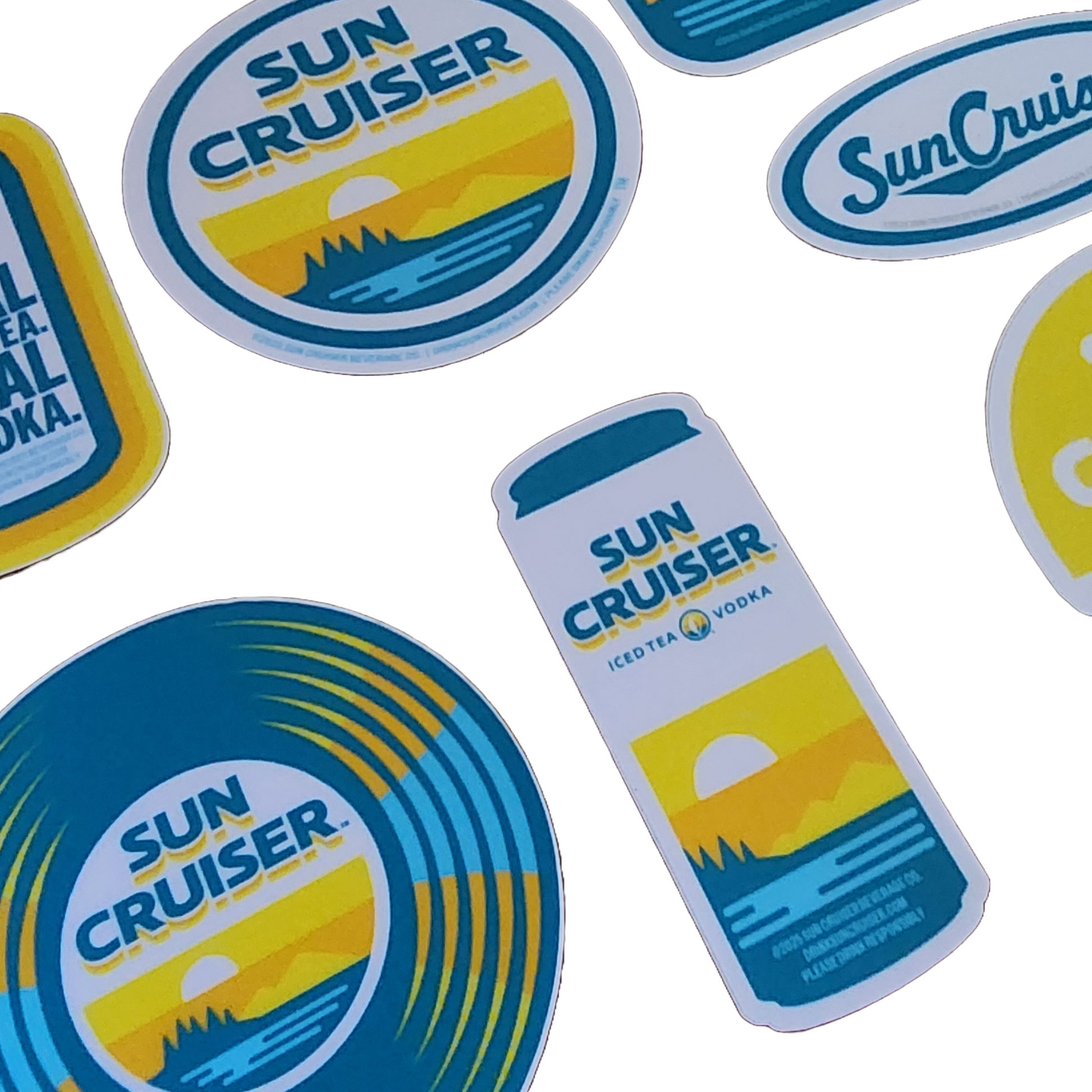 A collection of seven Sun Cruiser themed stickers of various shapes and colors is displayed. These include rectangular stickers with text and graphics of sunsets over mountains, a round sticker with a beach scene, an oval sticker with script text, and a can-shaped sticker with product details.