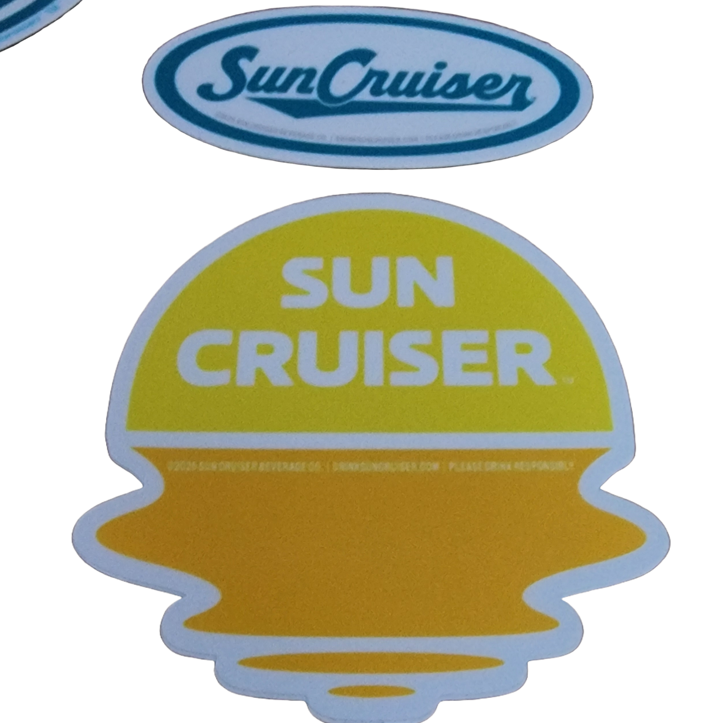 A collection of Sun Cruiser themed stickers of various shapes and colors is displayed on a light grey background, featuring branding and graphics like sunsets over landscapes.